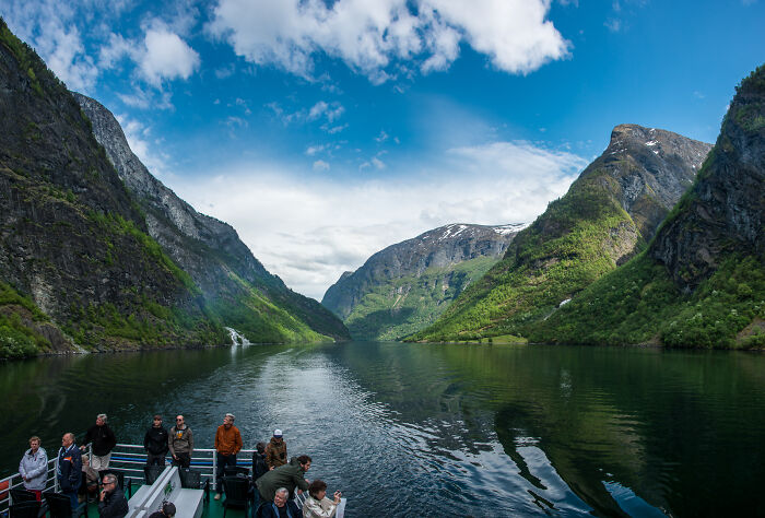 Tourists on a boat exploring hidden UNESCO gems surrounded by green mountains and a serene fjord under a partly cloudy sky.