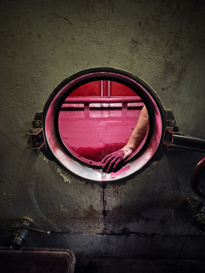Hand wearing a glove reaching into a vat with red liquid, showcasing creative world food photography award-winning shot.