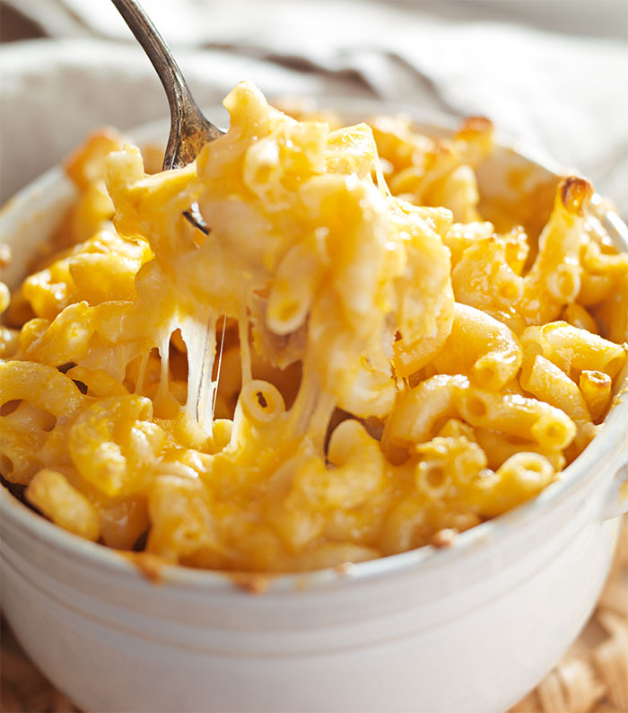 Baked macaroni and cheese with melted cheese being lifted by a fork, illustrating food stealing revenge concept.