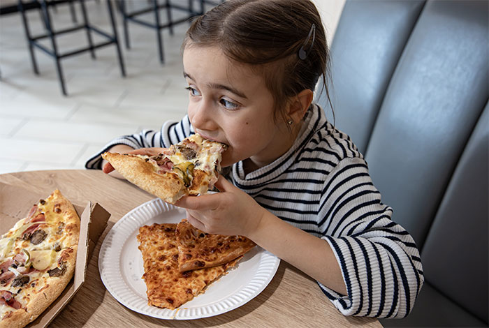 Young girl eating pizza at a table, illustrating a kid outing related to refusing outings with brother&rsquo;s kids.