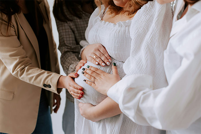Pregnant woman with friends touching baby bump during a moment focused on pregnancy announcement and family gathering.