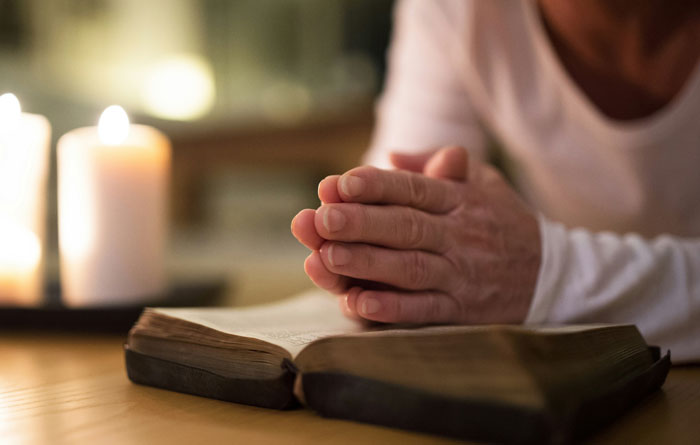 Person with hands clasped over an open book, lit by candles, symbolizing escape from cults and personal reflection.