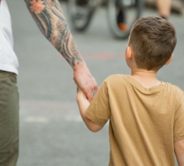 Adult with tattooed arm holding hands with child in brown shirt, symbolizing curiosity and fascinating today I learned facts.