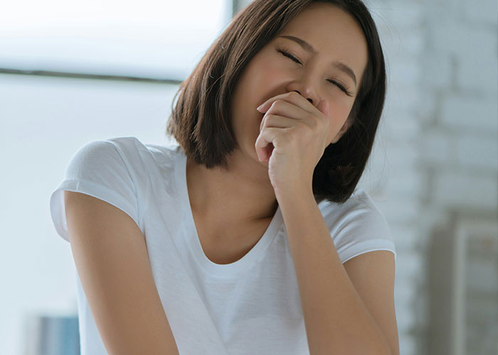Young woman in a white shirt covering her mouth, expressing discomfort from a pathetic injury she experienced.