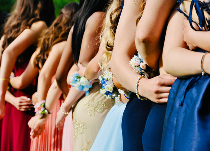 Teen girls dressed for prom stand side by side, wearing corsages and formal gowns in various colors.