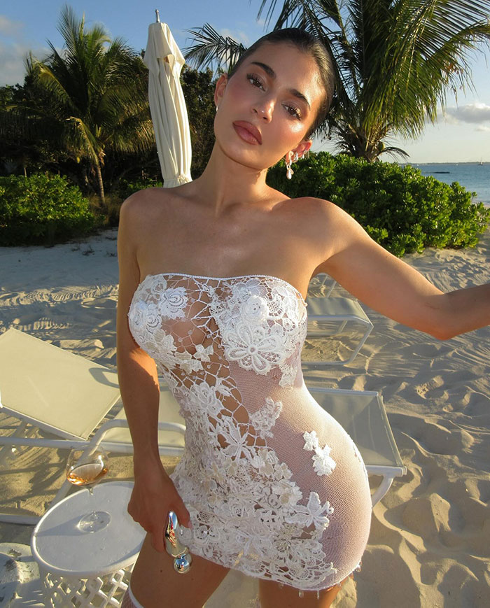 Kylie Jenner posing outdoors in a white low-cut dress with floral lace, sparking fan concern on social media.