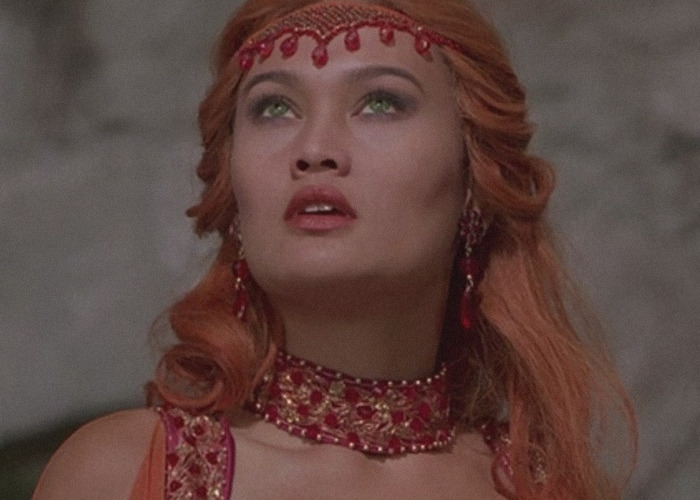 Tia Carrere in a detailed costume with red and gold accents, showcasing her '90s icon style and timeless beauty.