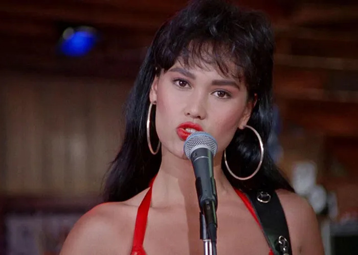 Tia Carrere singing on stage with large hoop earrings and red dress, 90s icon known for timeless beauty and style
