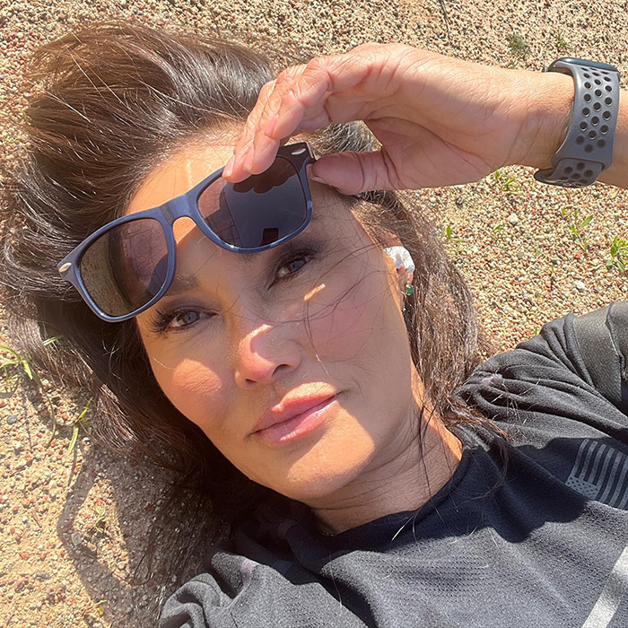 Tia Carrere close-up selfie outdoors, wearing black shirt and sunglasses, showcasing her youthful look and natural beauty.