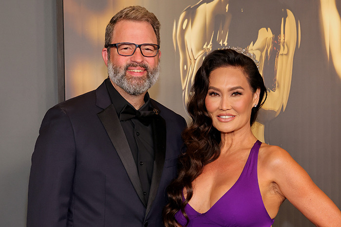 Tia Carrere in a plunging purple gown posing with a man in a black suit at a formal event.