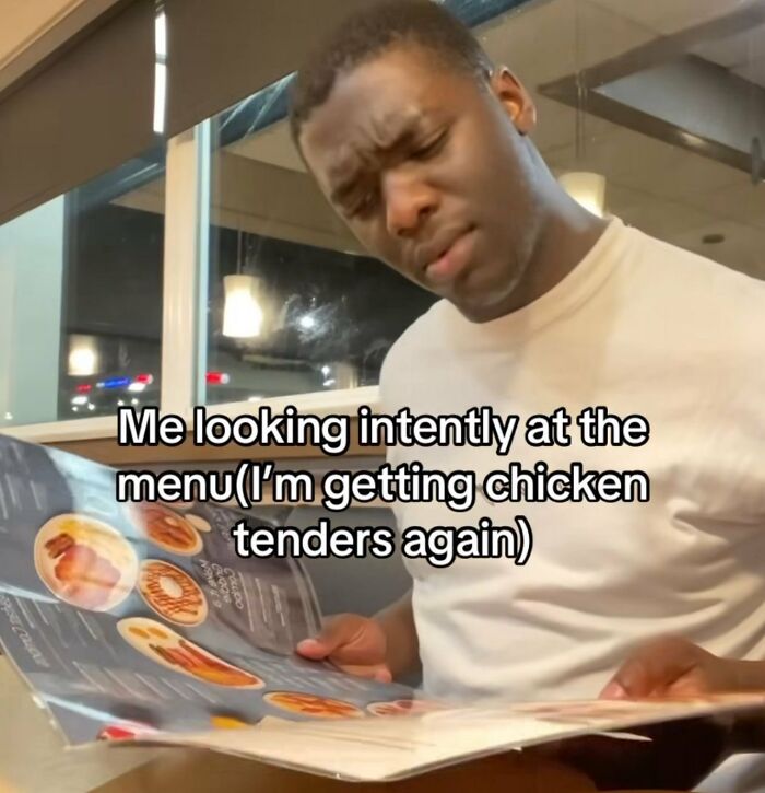Young man looking intently at a restaurant menu, illustrating chaotic memes about indecision and repetitive choices.
