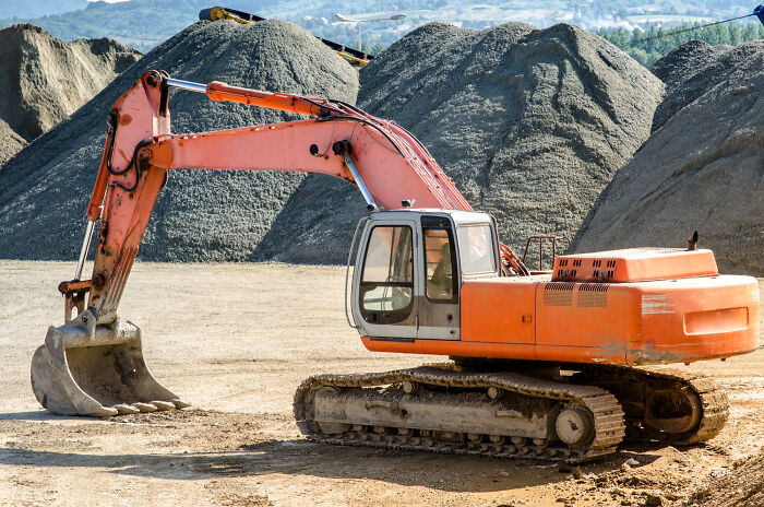 Orange excavator on construction site with gravel piles, illustrating casual things that can actually be deadly.