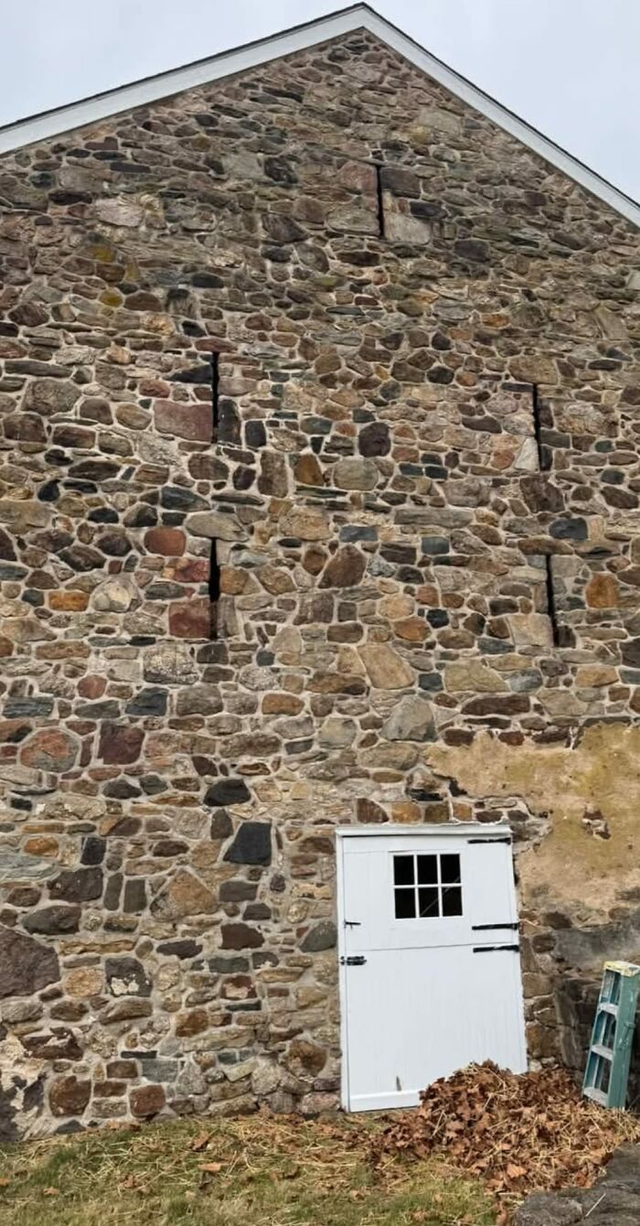 Stone exterior wall of an old home with hidden narrow openings and a white door, showing strange features in homes with hidden pasts.