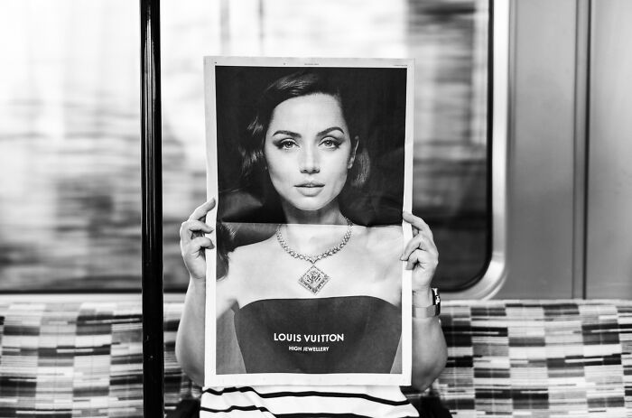 Person holding Louis Vuitton ad poster in front of face, captured in black and white street photography style.