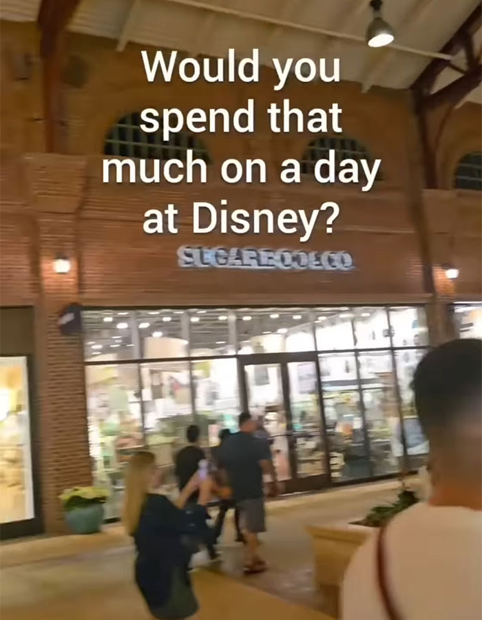 People walking outside a store with text asking if spending that much on a day at Disney is really worth it family trip debate. People walking outside a store with text asking if spending that much on a day at Disney is really worth it family trip debate.