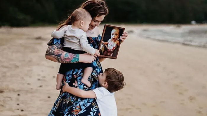 Woman holding two young children and a framed photo of a baby, reflecting on a tragic babysitter Benadryl incident.