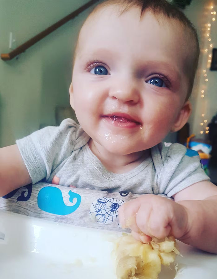 Smiling baby sitting in high chair holding food, related to fatal Benadryl dose given by babysitter case.