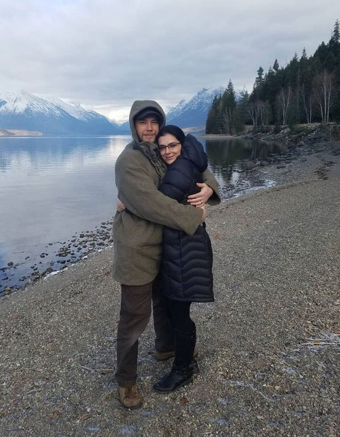 Couple embracing on a rocky lakeshore with snowy mountains and pine trees in the background in Montana outdoors. Couple embracing on a rocky lakeshore with snowy mountains and pine trees in the background in Montana outdoors.
