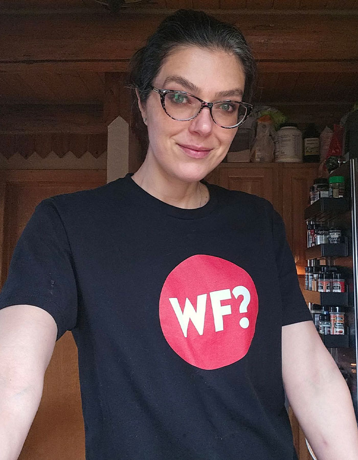 Woman with glasses wearing black shirt with WF logo, standing indoors in a kitchen selling Avon in Montana after modeling career. Woman with glasses wearing black shirt with WF logo, standing indoors in a kitchen selling Avon in Montana after modeling career.