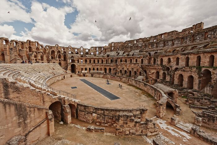 Ancient stone amphitheater under cloudy sky showcasing hidden UNESCO gems with historic architecture and few visitors.