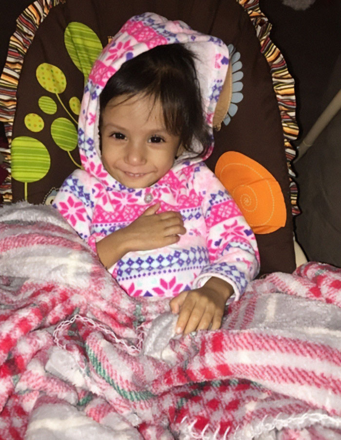 Young child wrapped in blankets, wearing a pink patterned hooded sweater, highlighting mom who locked starving child in closet.