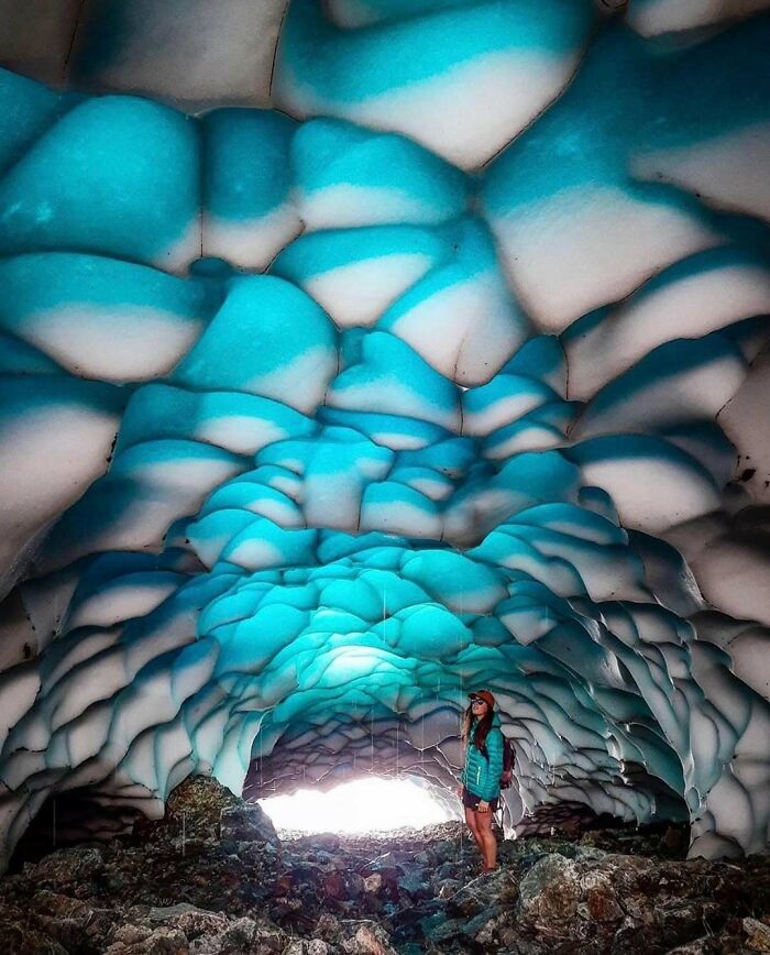 Person standing inside a vibrant blue and white ice cave showcasing rare natural phenomena and stunning geological formations.