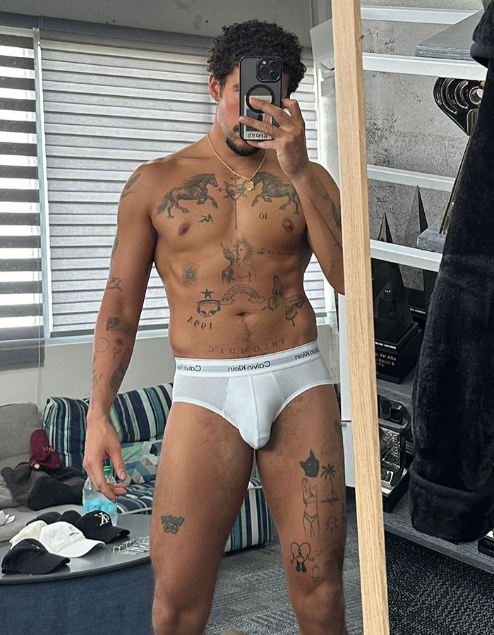 Bad Bunny shirtless selfie in white Calvin Klein underwear, showing tattoos and posing in a bedroom mirror.