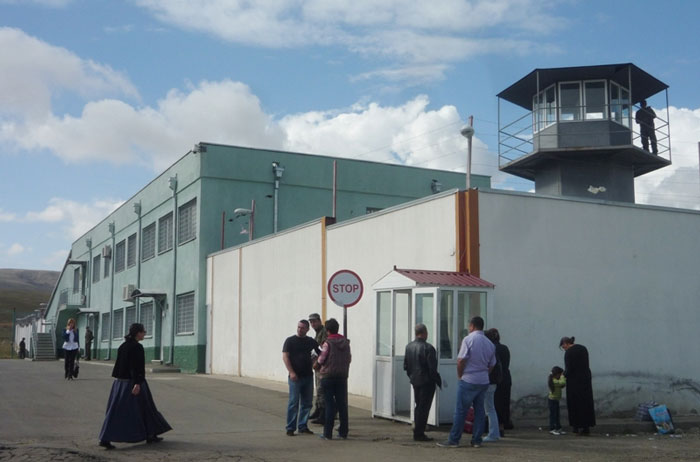 Group of people gathered outside a secured facility with a watchtower under a partly cloudy sky in Thailand.