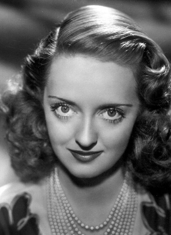 Black and white portrait of a glamorous 1940s icon with styled hair and pearl necklace representing Hollywood elegance.