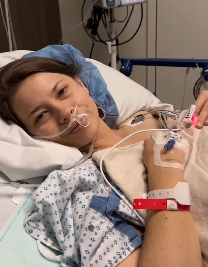 Bindi Irwin lying in hospital bed with oxygen tube, showing health update after medical emergency from incurable disease.