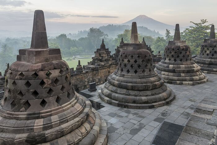 Ancient stone stupas at a hidden UNESCO site with a misty forest and mountain in the background at sunrise.