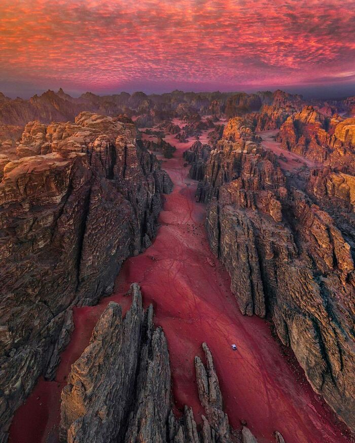Aerial view of rocky canyon landscape under vibrant red and orange sky, capturing rare natural phenomena at sunset.