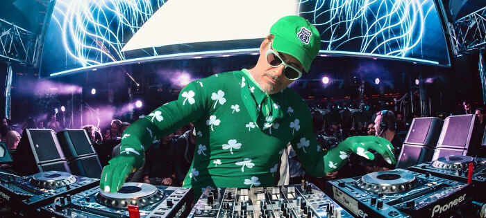 Man wearing green shamrock outfit and cap DJing at a club, showcasing creative and hilarious Photoshop skills artwork.