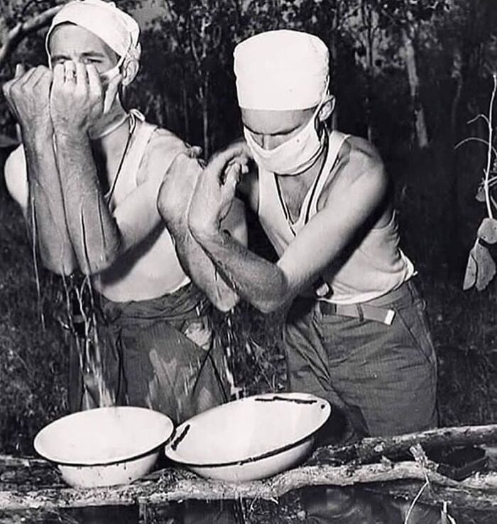 Two masked medical personnel washing arms outdoors before surgery, illustrating uncanny moments in medicine history.