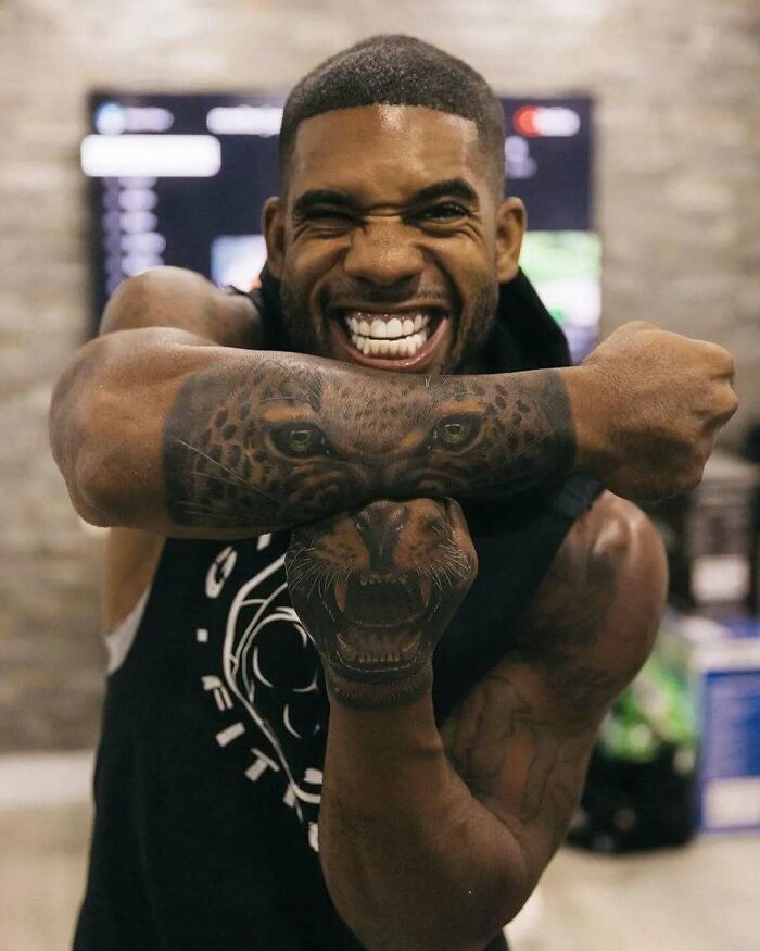 Hombre sonriente mostrando tatuajes de leopardo en brazo y mano, ejemplo de tatuajes que van desde lo gracioso hasta lo terrible.