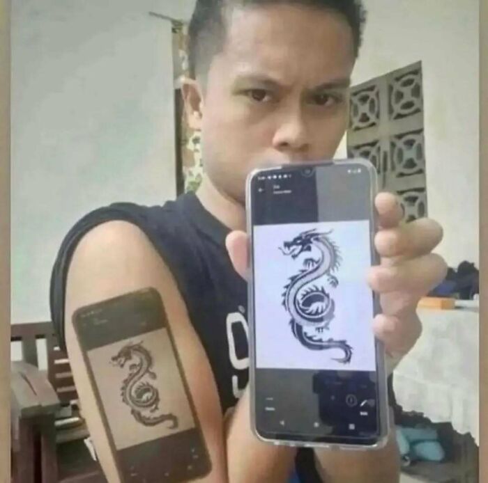 Man showing a funny tattoo of a phone displaying a dragon design, highlighting interesting and bad tattoos.