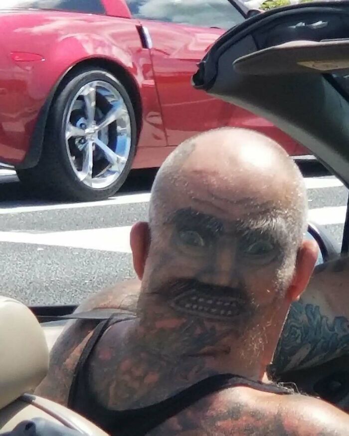 Man with a funny and interesting tattoo on the back of his head creating a face illusion while sitting in a car.