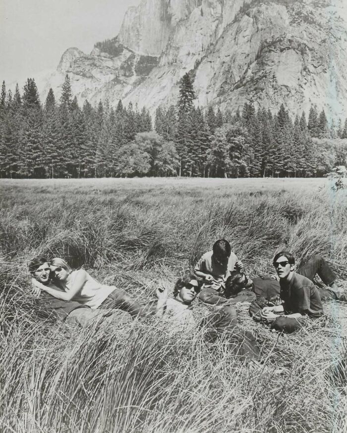 Group of friends relaxing in a field with trees and mountains in the background in a vintage photo showing history.