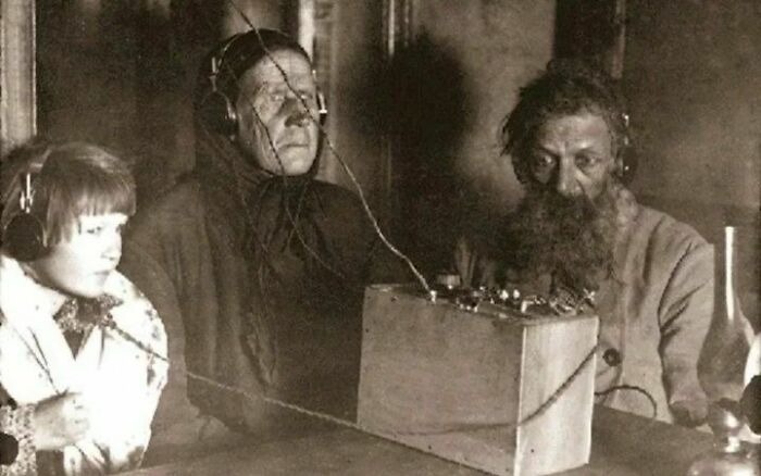 Three people wearing headphones using early radio equipment in a vintage photo showing history up close.