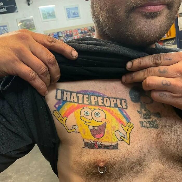 Tatuaje colorido de Bob Esponja en el pecho con texto irónico, ejemplo de tatuajes que van de lo gracioso a lo terrible.