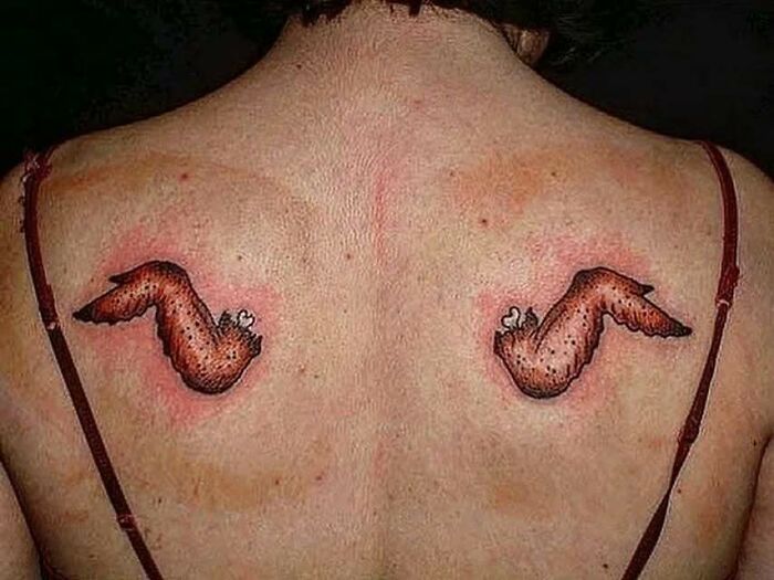 Two funny and interesting tattoos of cartoonish wings on a person’s upper back with red irritated skin around them.