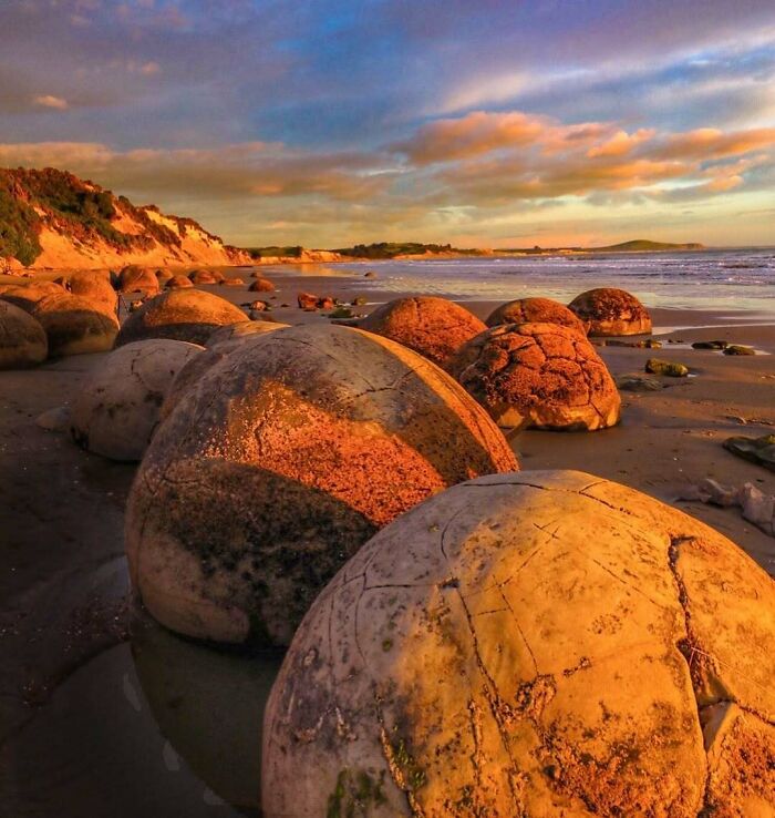 Large spherical rocks on a sandy beach under a colorful sky, showcasing rare natural phenomena in nature photography.