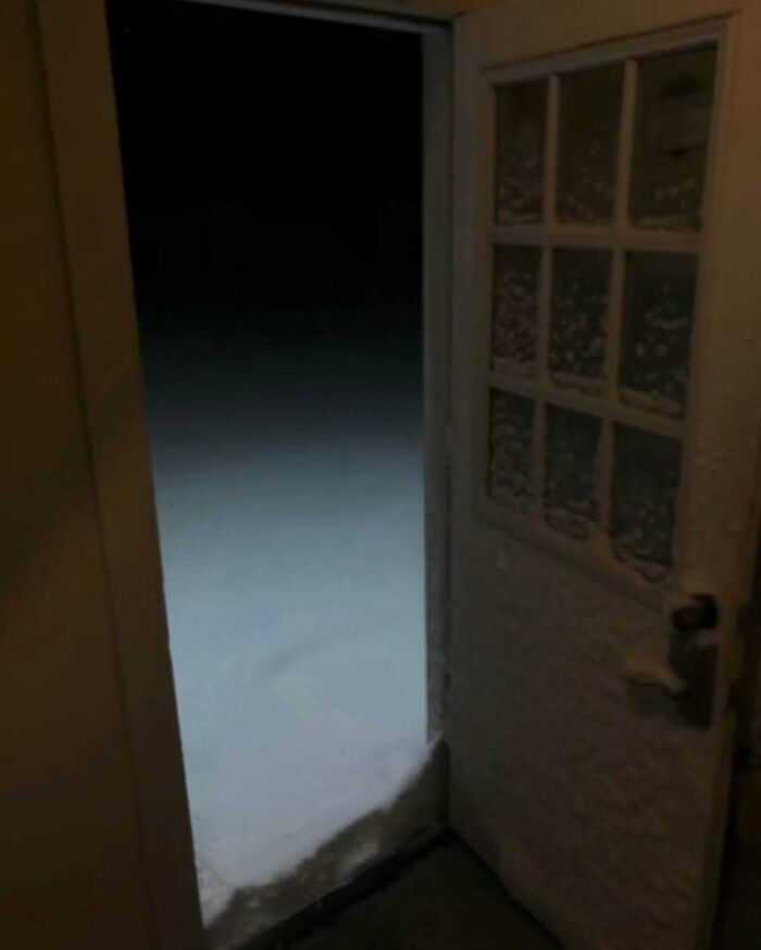 Open door revealing unsettling yet fascinating empty snowy space beyond in dim lighting.