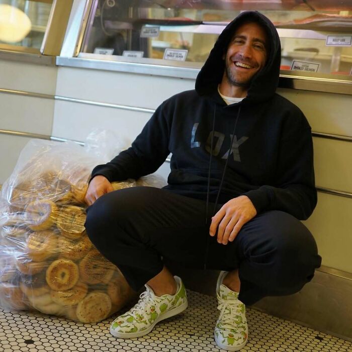 Man in a black hoodie crouching next to a large bag of bagels, illustrating celebrities called out for hygiene habits.
