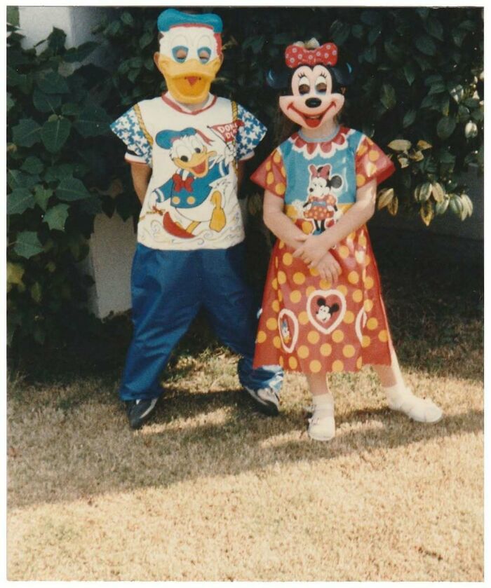 Two children dressed in vintage Donald Duck and Minnie Mouse costumes standing outdoors on grass.