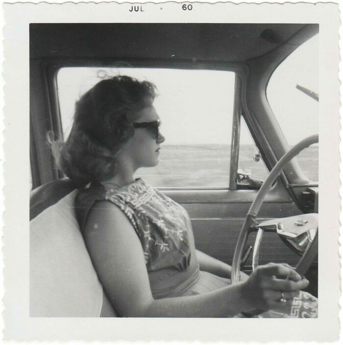 Vintage photo of a woman wearing sunglasses, driving a car in the 1960s, showcasing mesmerizing history moments.