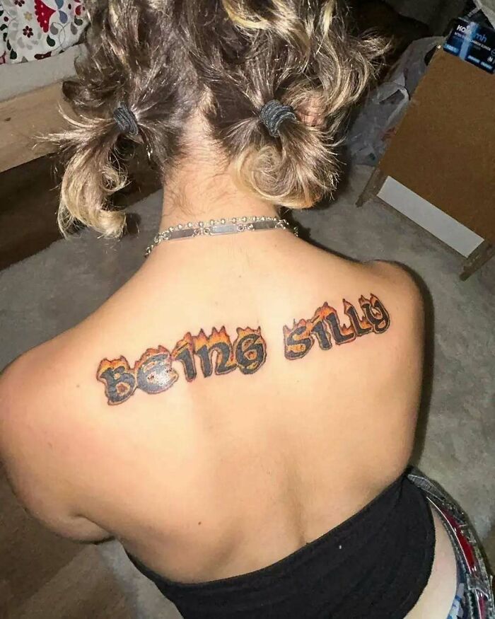 Tattoo on upper back with words being silly in flaming, bold lettering, showcasing funny and interesting tattoo design.