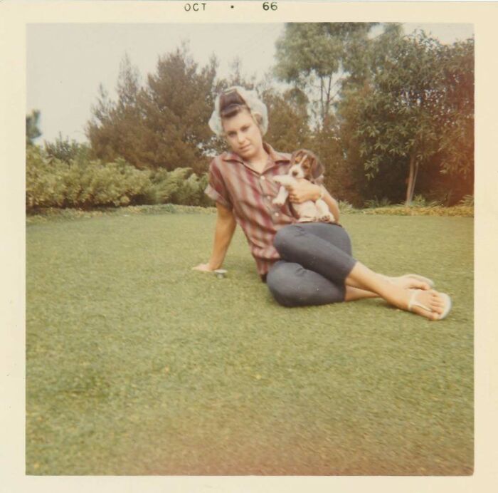Vintage photo from 1966 showing a woman sitting on grass holding a puppy, capturing a nostalgic moment in history.