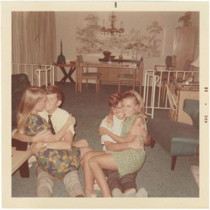 Two vintage couples embracing and smiling on a living room floor in a cozy 1960s home setting.