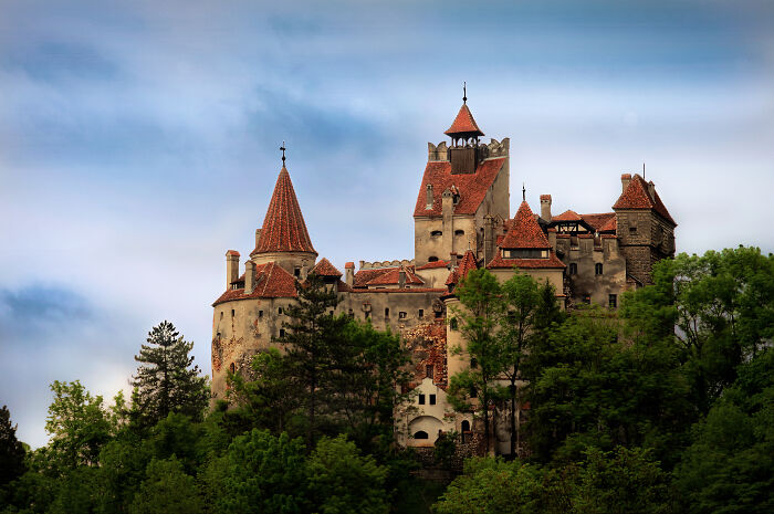 Medieval castle surrounded by trees under a cloudy sky representing national stereotypes and historic architecture.